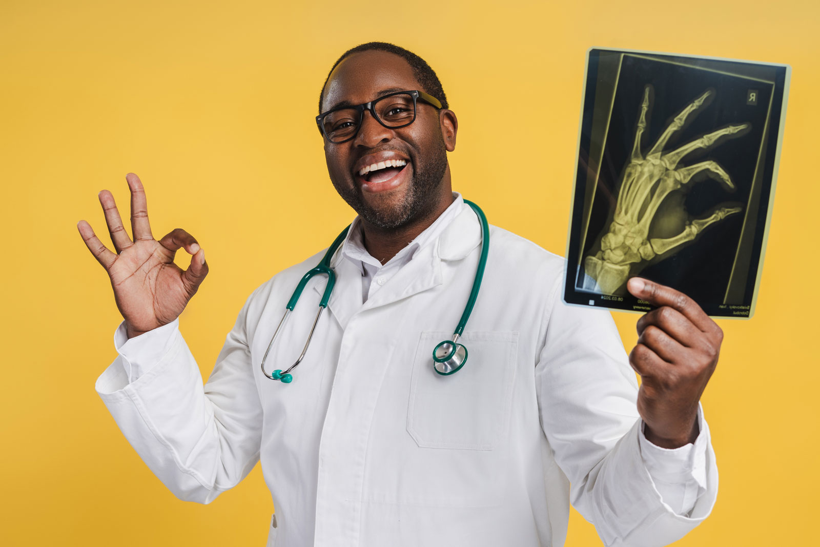 Smiling African American doctor holding X-ray picture with ok gesture, isolated on yellow